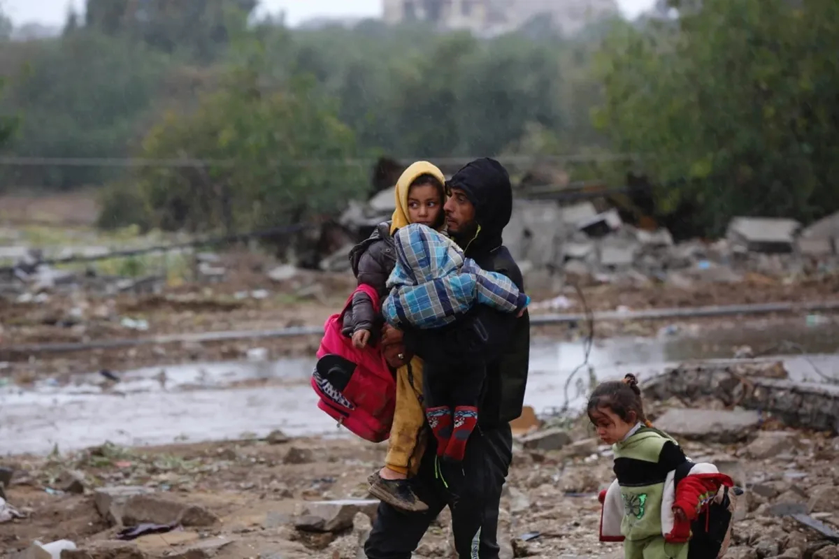 Палестинец несет детей в секторе Газа во время гуманитарной паузы, 27 ноября 2023 года. Фото: БАПОР / Ашраф Амра